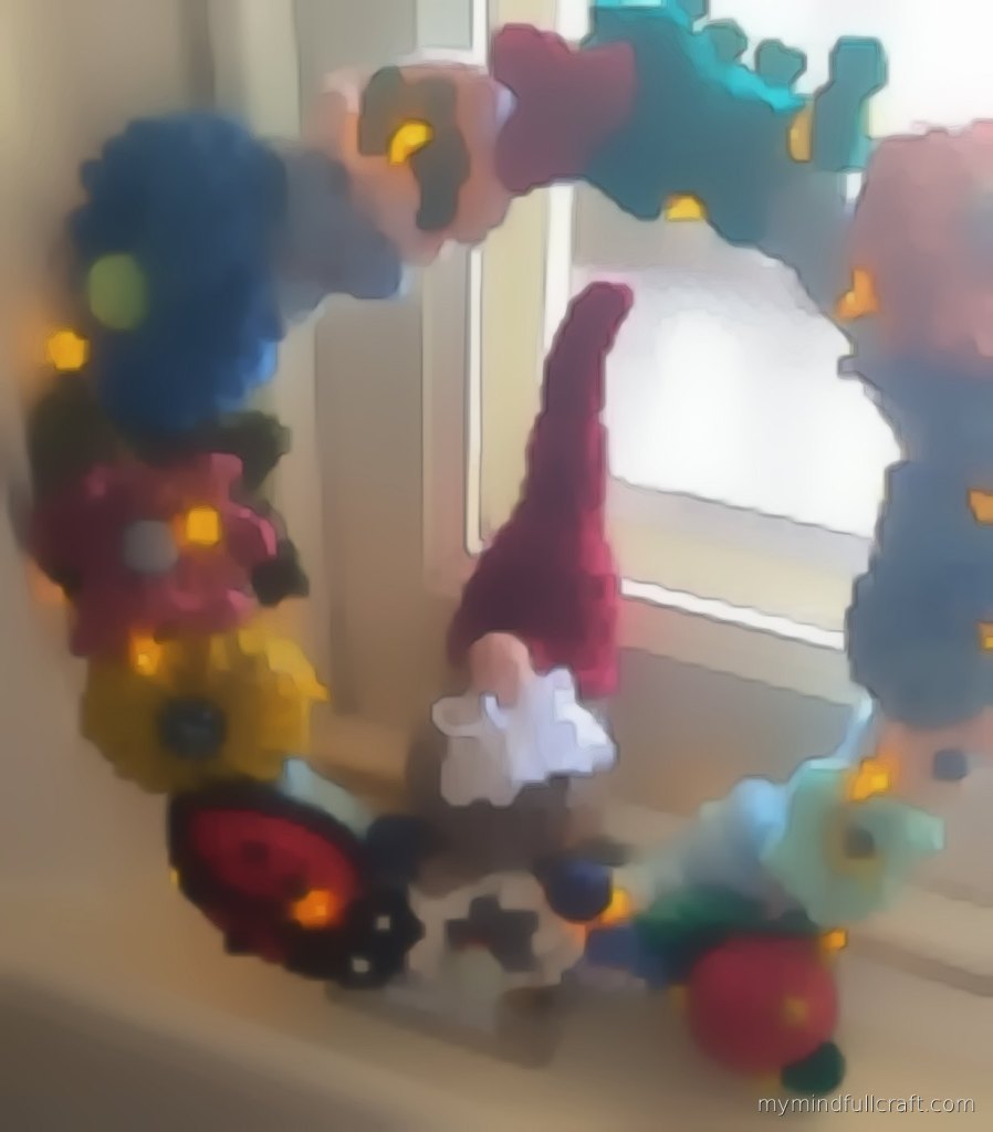 A student's crocheted wreath with a gnome, ladybird, flowers and warm fairy lights on a windowsill